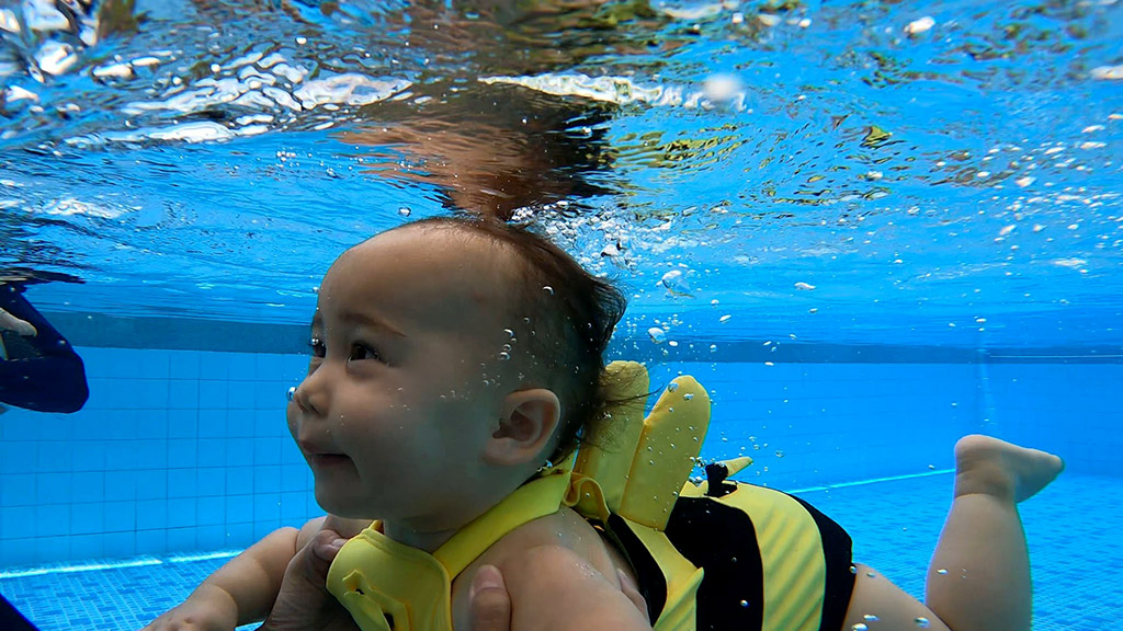 cute baby in a bee swimming costume under water in a swimming lesson